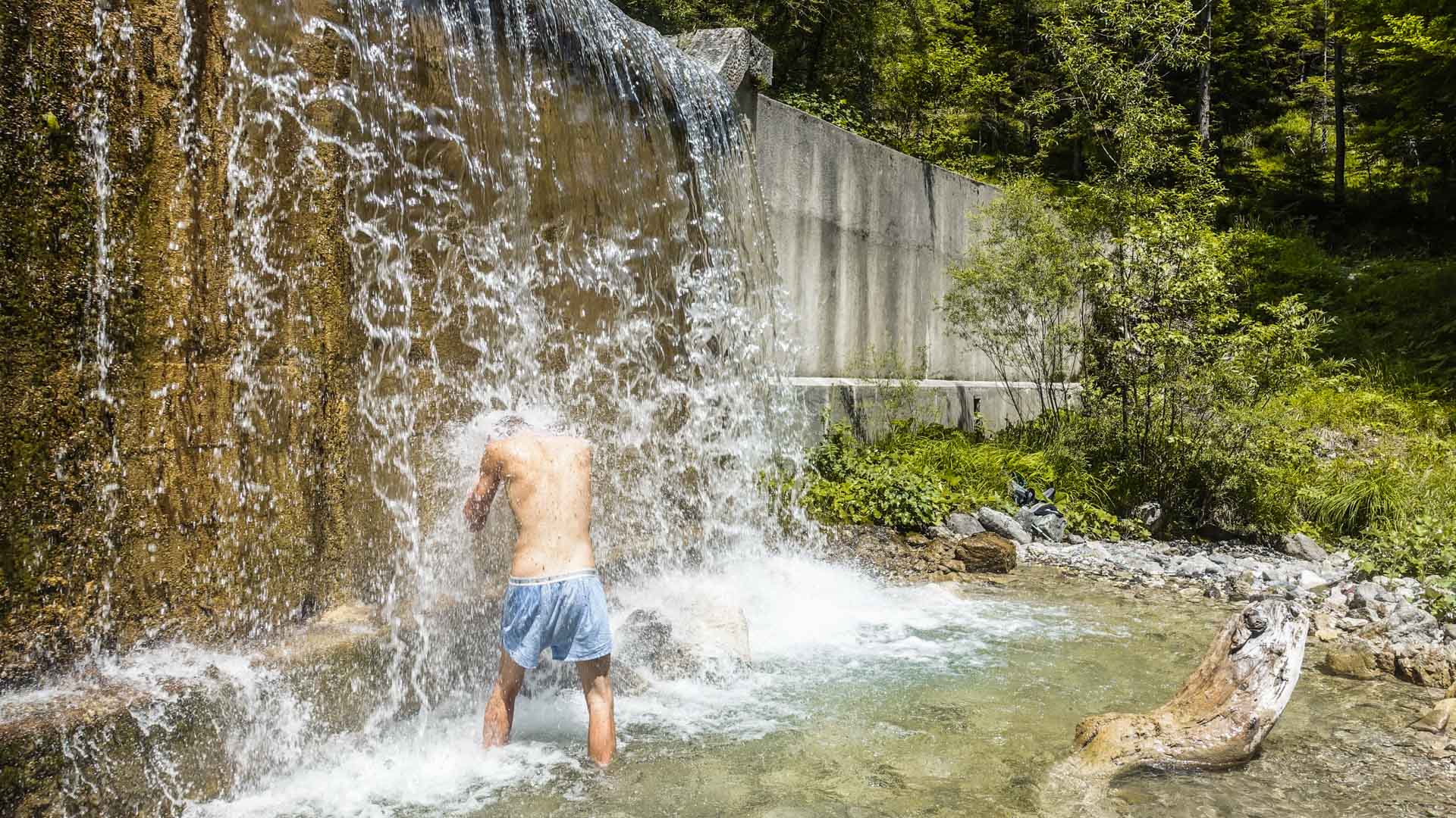 Bergwanderer steht oberkörperfrei unter einem Wasserfall am Bartolo Bach in Slowenien im Sommer.