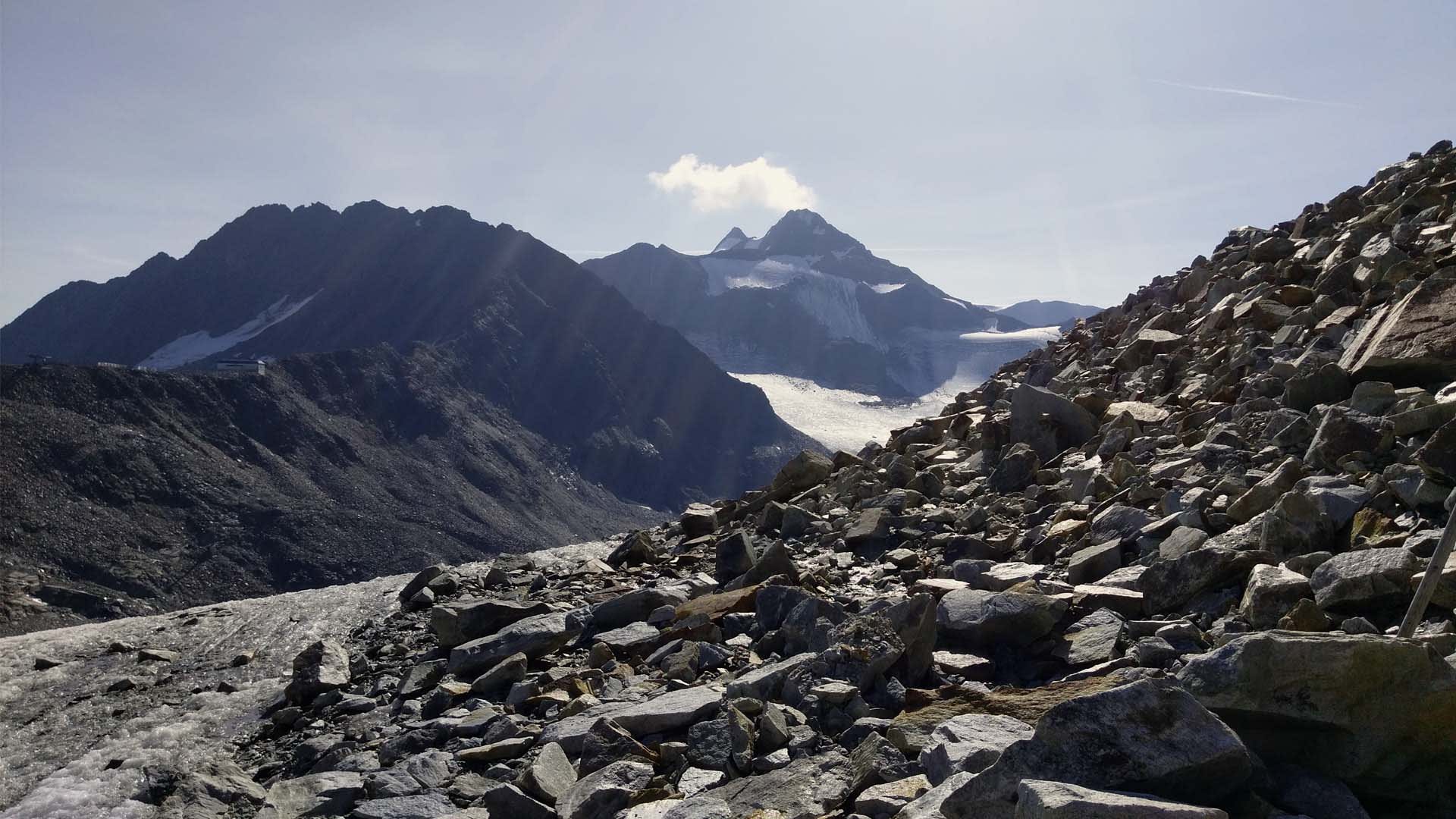 Bergwanderung auf der Alpenüberquerung Zugspitze–Meran: Geröllfeld mit Gletscherblick und Schutzhütte im Talkessel.