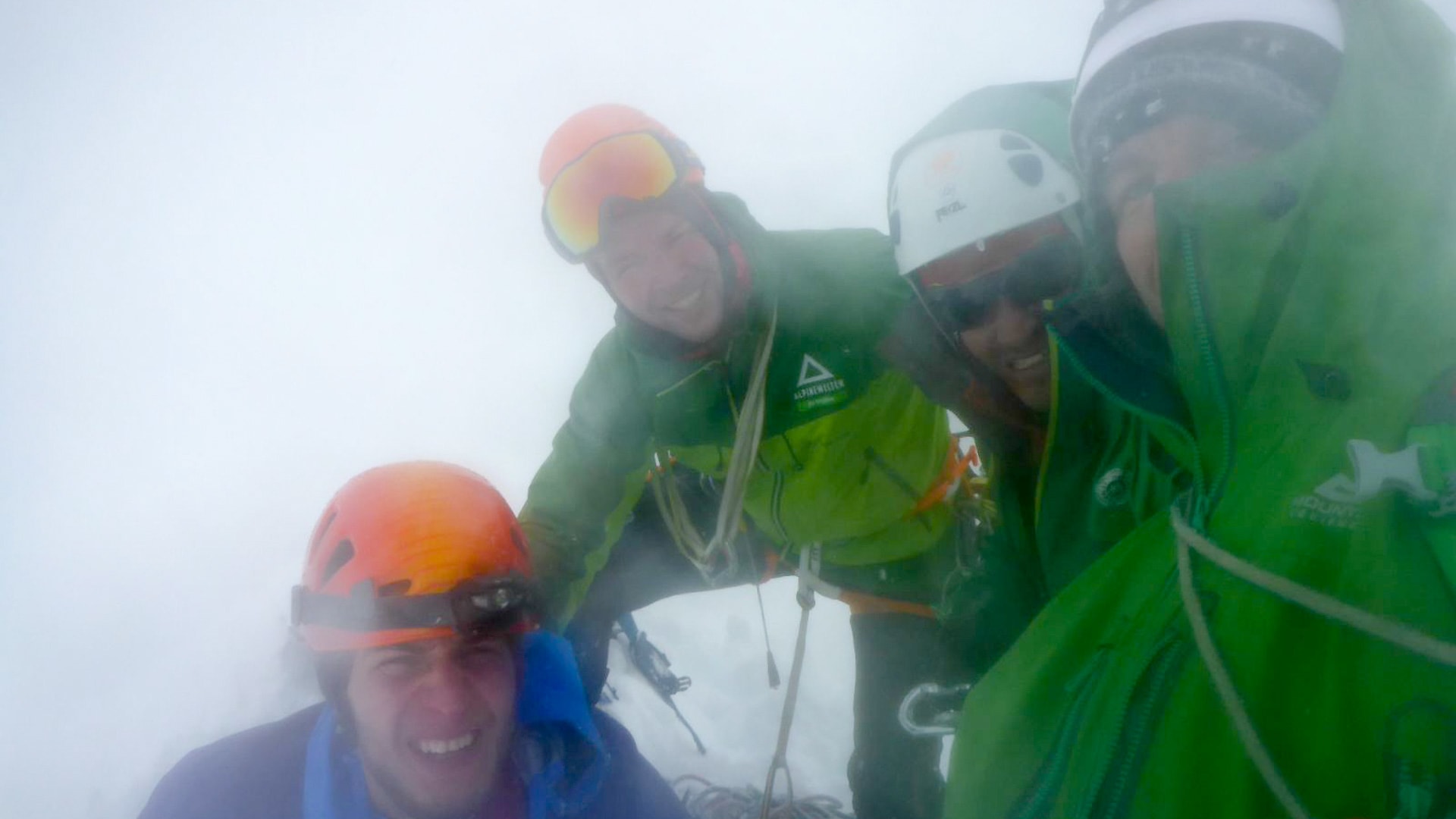 Expedition Alpamayo: vier Höhenbergsteiger mit Helmen und Seilen im dichten Nebel auf dem Gipfel.