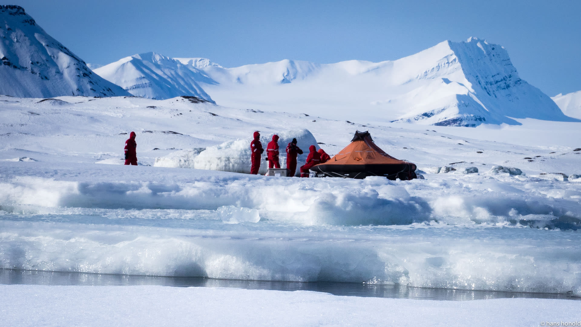 Expedition auf Spitzbergen: fünf Höhenbergsteiger in roten Schutzanzügen neben Rettungsinsel und Schneebau auf Packeis.