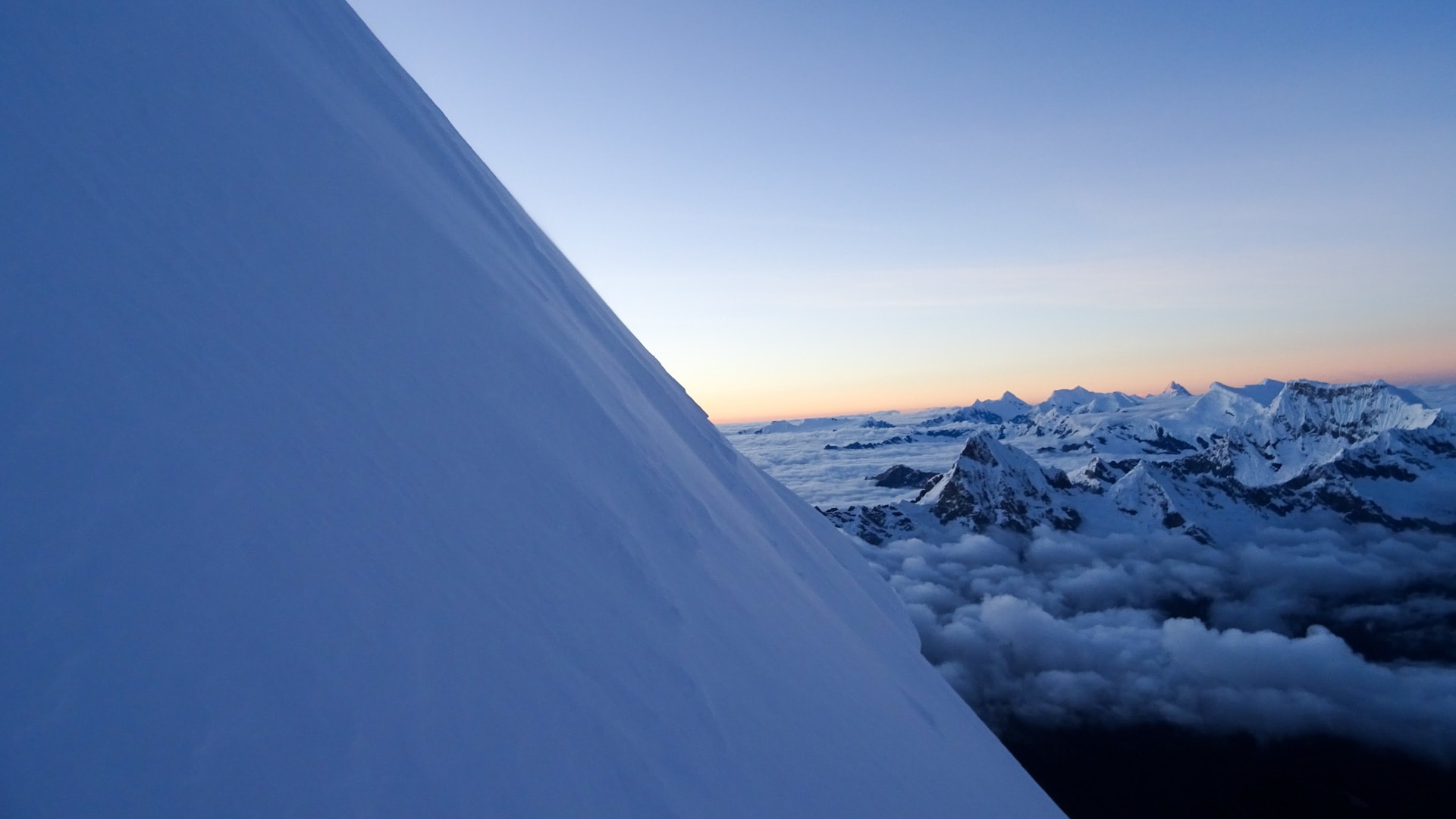 Expedition am Chopicalqui: steile Südwestflanke aus großer Höhe mit Blick über Wolkenmeer auf Andengipfel.