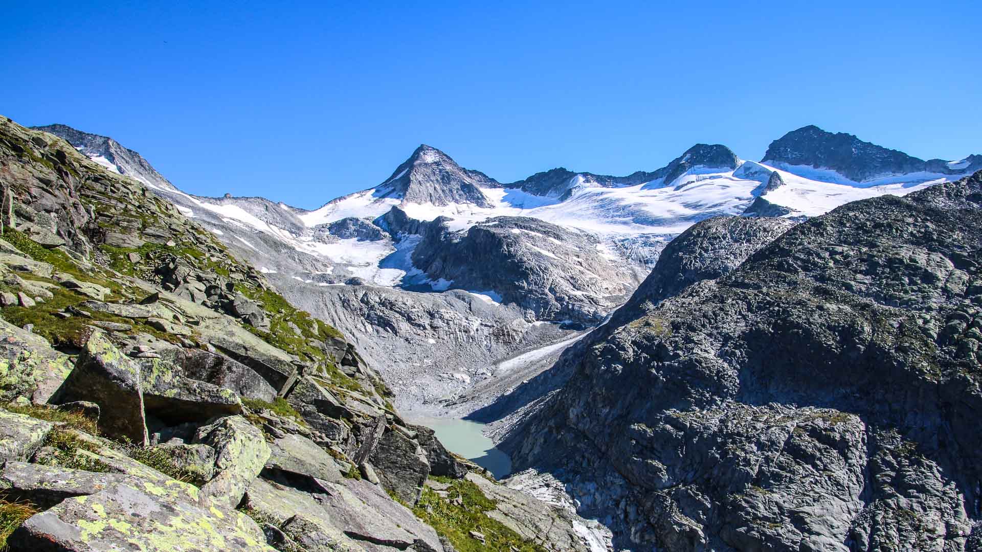 Hochtour am Großvenediger: milchig-türkiser Gletschersee im Felskessel mit pyramidenförmigem Gipfel und Schneefeldern