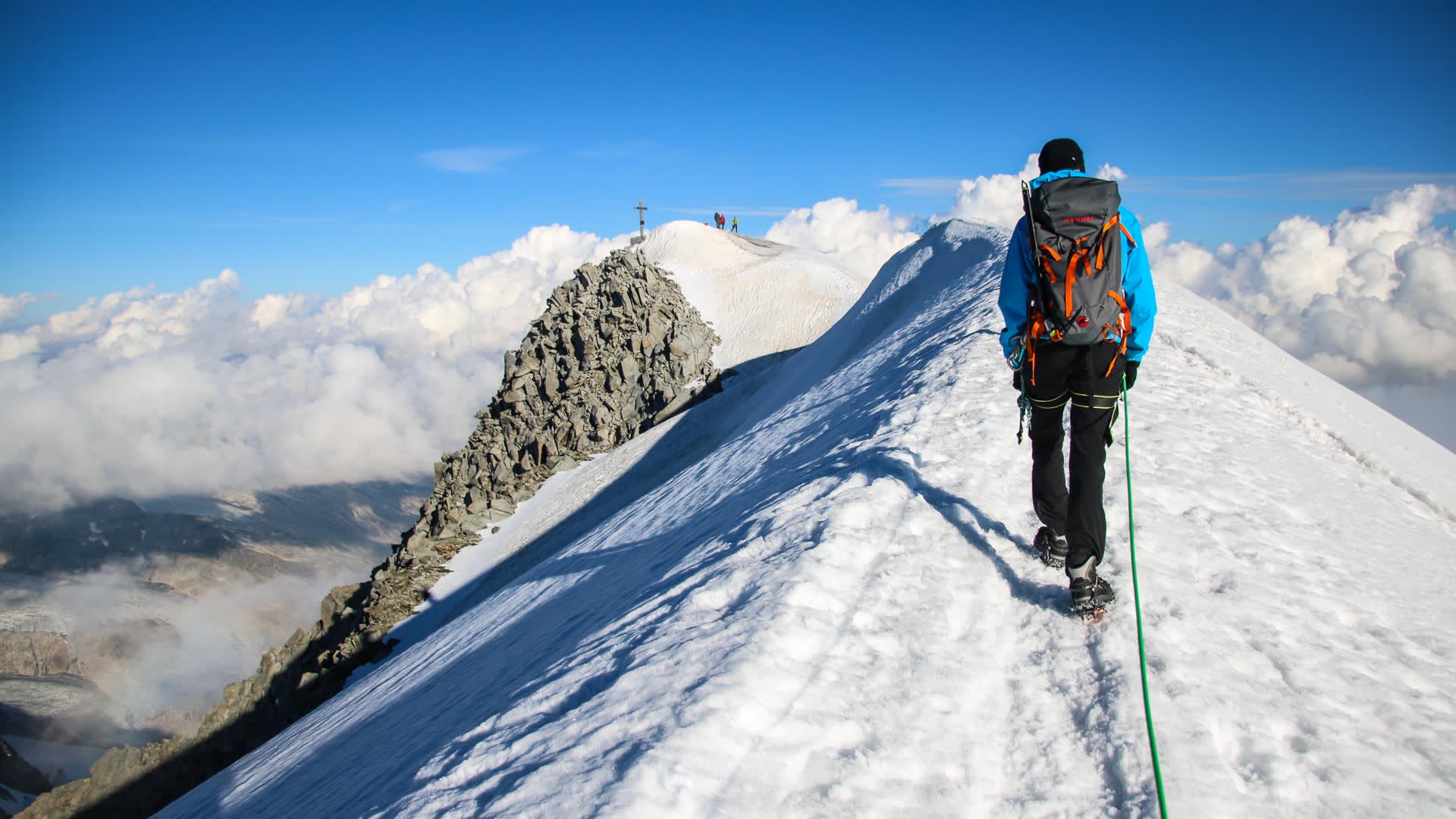 Hochtour am Großvenediger: Bergsteiger mit Steigeisen und Seilsicherung steigt über den Schneegrat zum Gipfelkreuz.