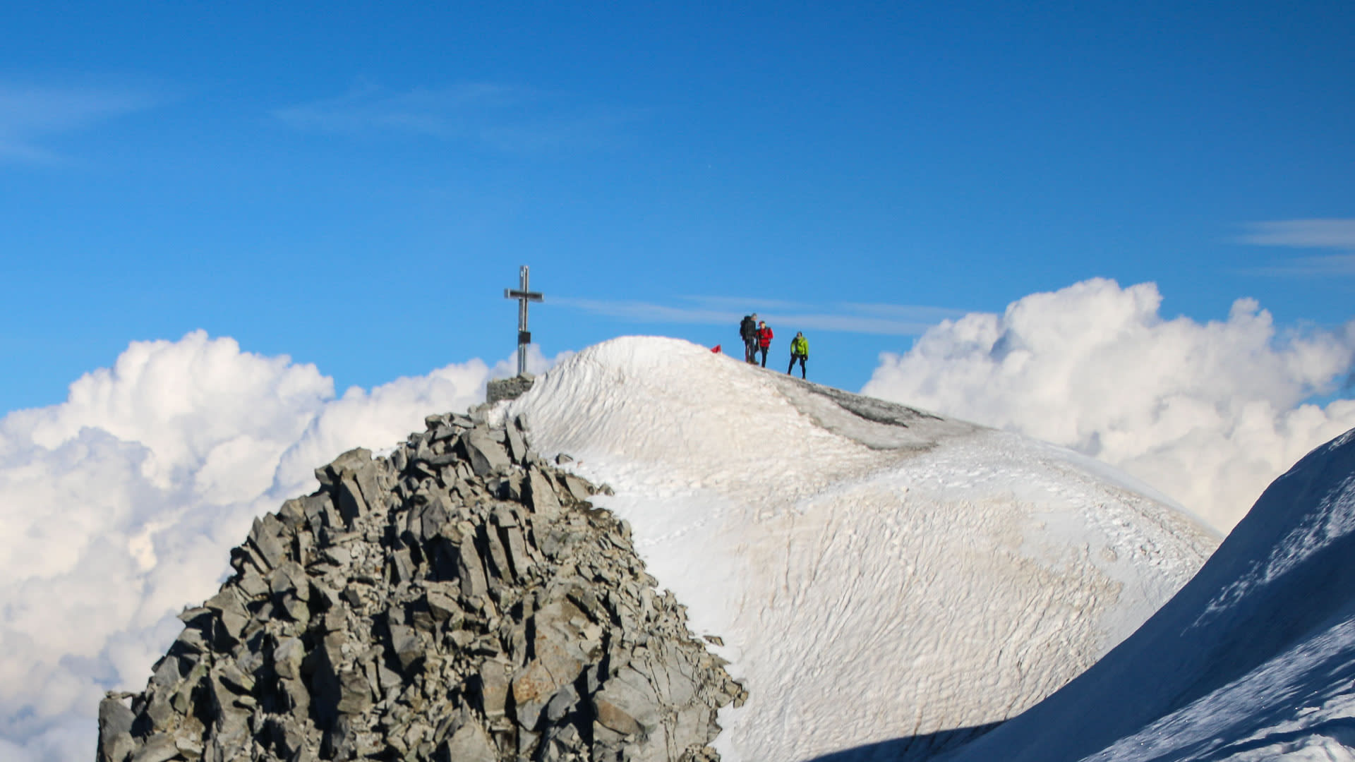 Hochtour auf den Großvenediger: drei Bergsteiger auf dem Schneegipfel neben dem Gipfelkreuz.