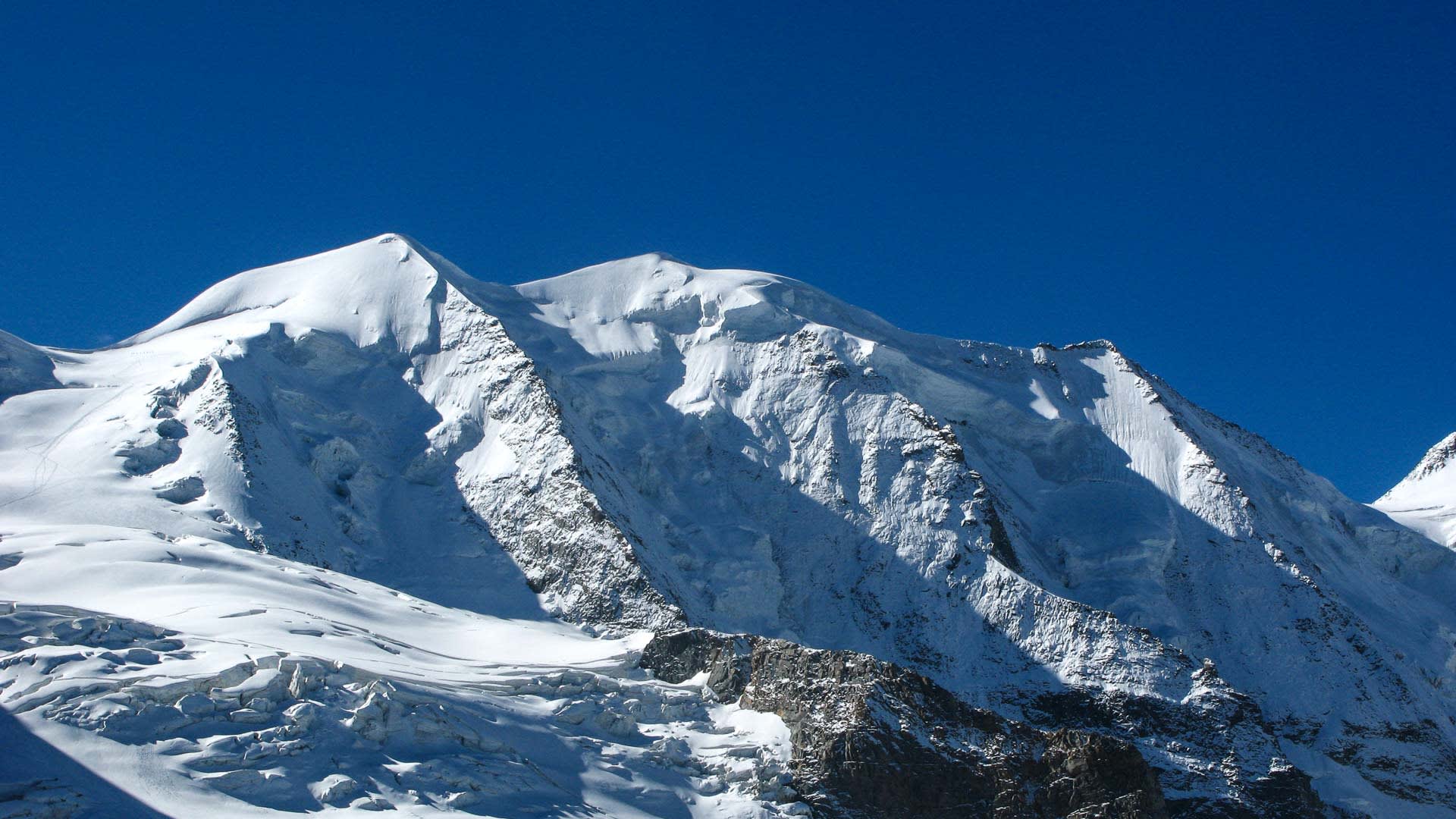 Hochtour Piz Palü: verschneites Doppelgipfelmassiv mit breitem Schneegrat, Seracs und felsigen Steilwänden im Vordergrund.
