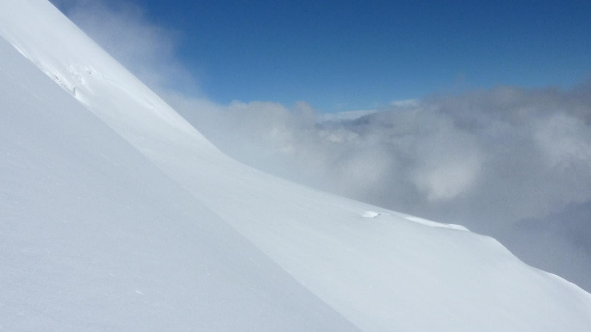 Hochtour Piz Palü: steiler Gletscherhang mit Aufstiegsspur über einem dichten Wolkenmeer, blauer Himmel im Bernina-Gebiet.