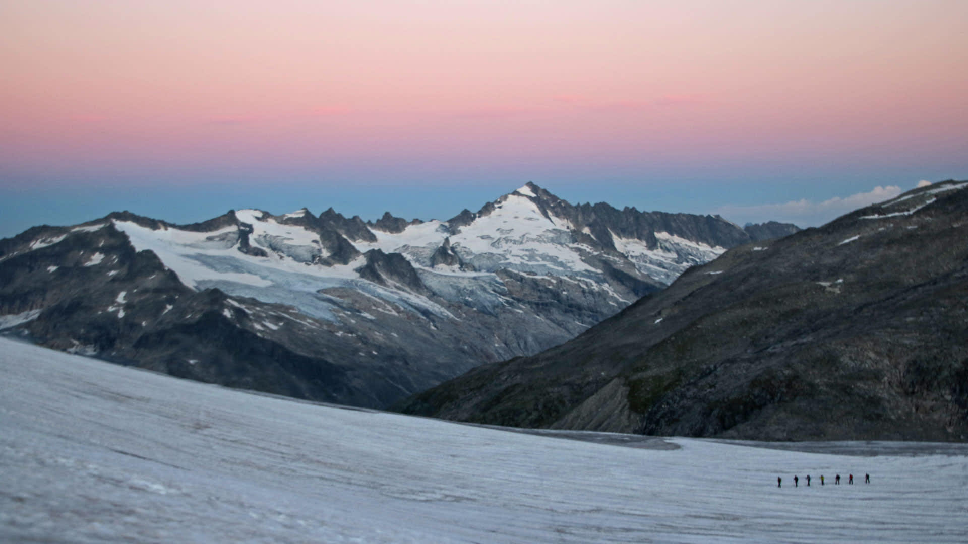 Hochtour zum Großvenediger: Bergsteigergruppe steigt in langer Reihe über einen flachen Gletscher im Morgenrot auf.