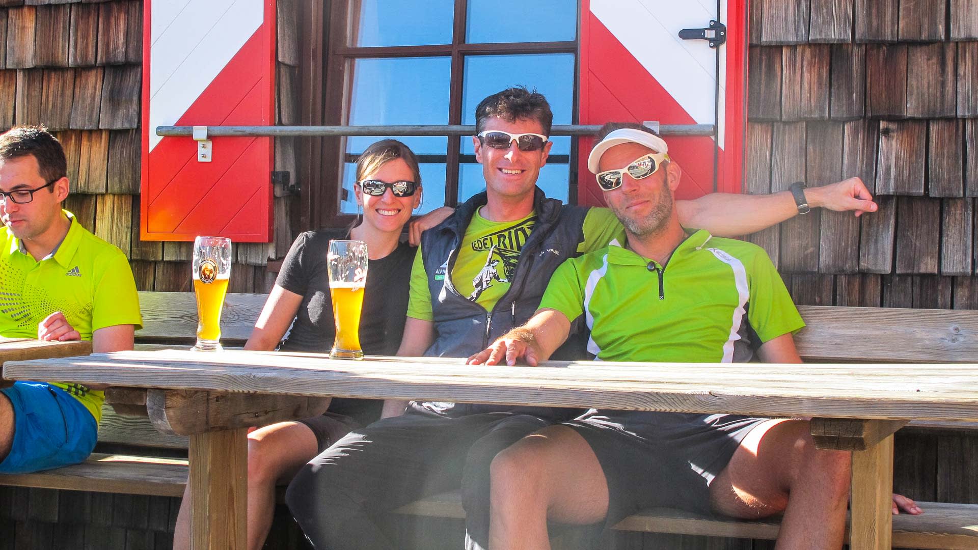 Vier Hochtour-Bergsteiger pausieren mit Getränken an einem Holztisch vor der Kürsinger Hütte am Großvenediger.