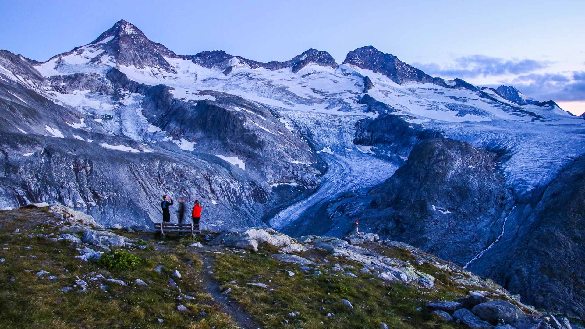Drei Bergsteiger stehen bei der Kürsinger Hütte am Großvenediger und blicken auf den Gletscher in der Dämmerung.