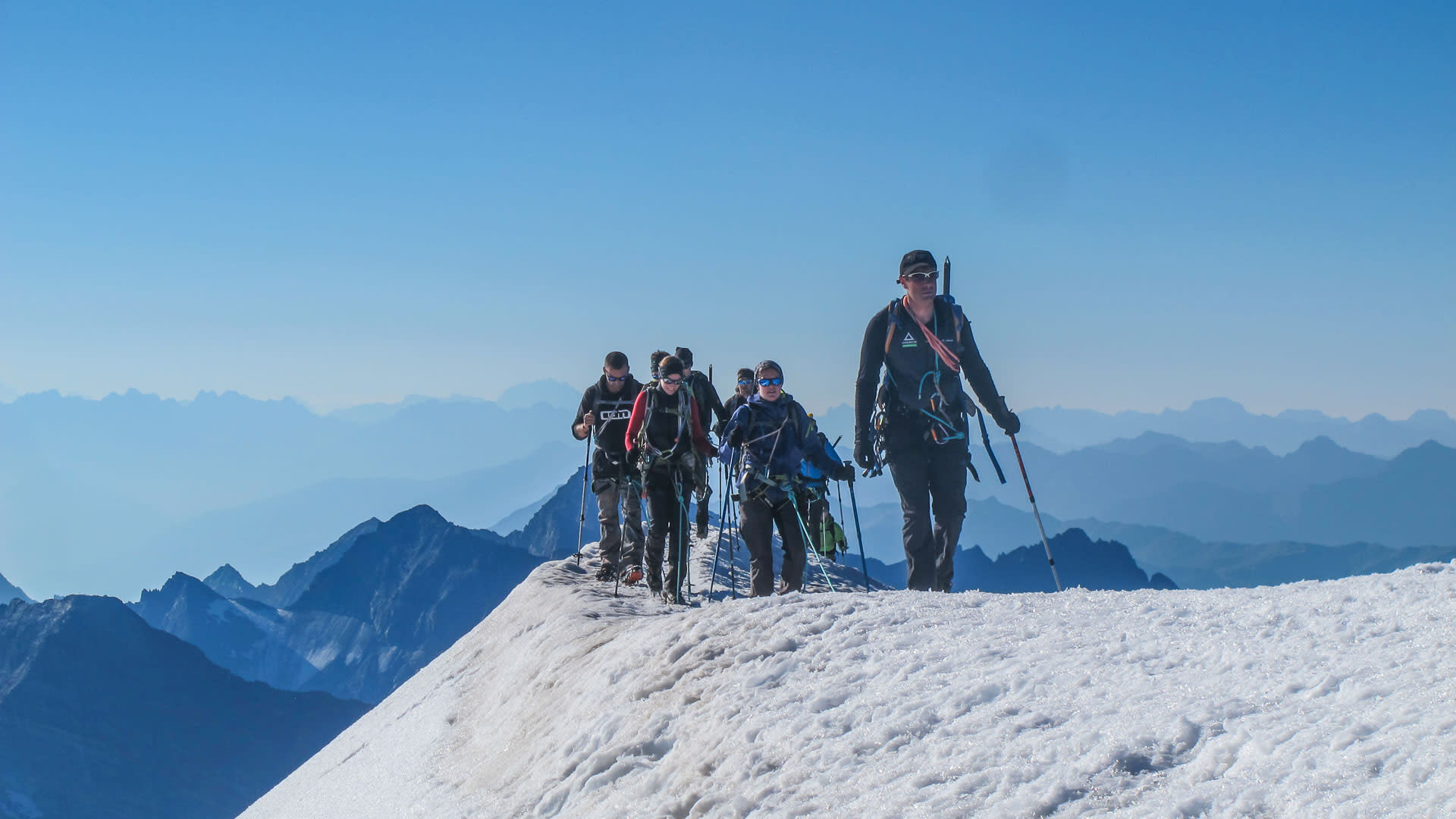 Hochtour Großvenediger: Bergsteigergruppe steigt mit Rucksäcken und Wanderstöcken einen steilen Schneegrat auf.