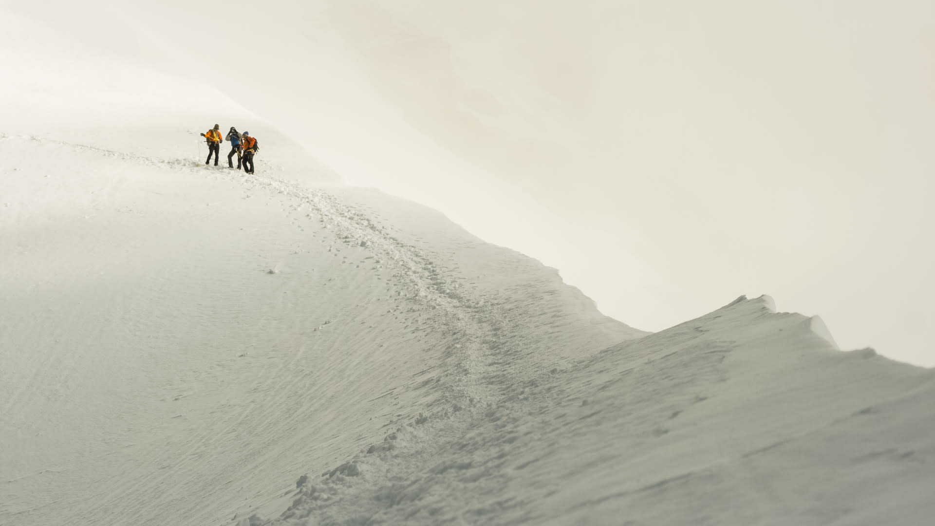 Drei Bergsteiger pausieren auf einem verschneiten Hang bei der Hochtour zur Jungfrau im Berner Oberland.