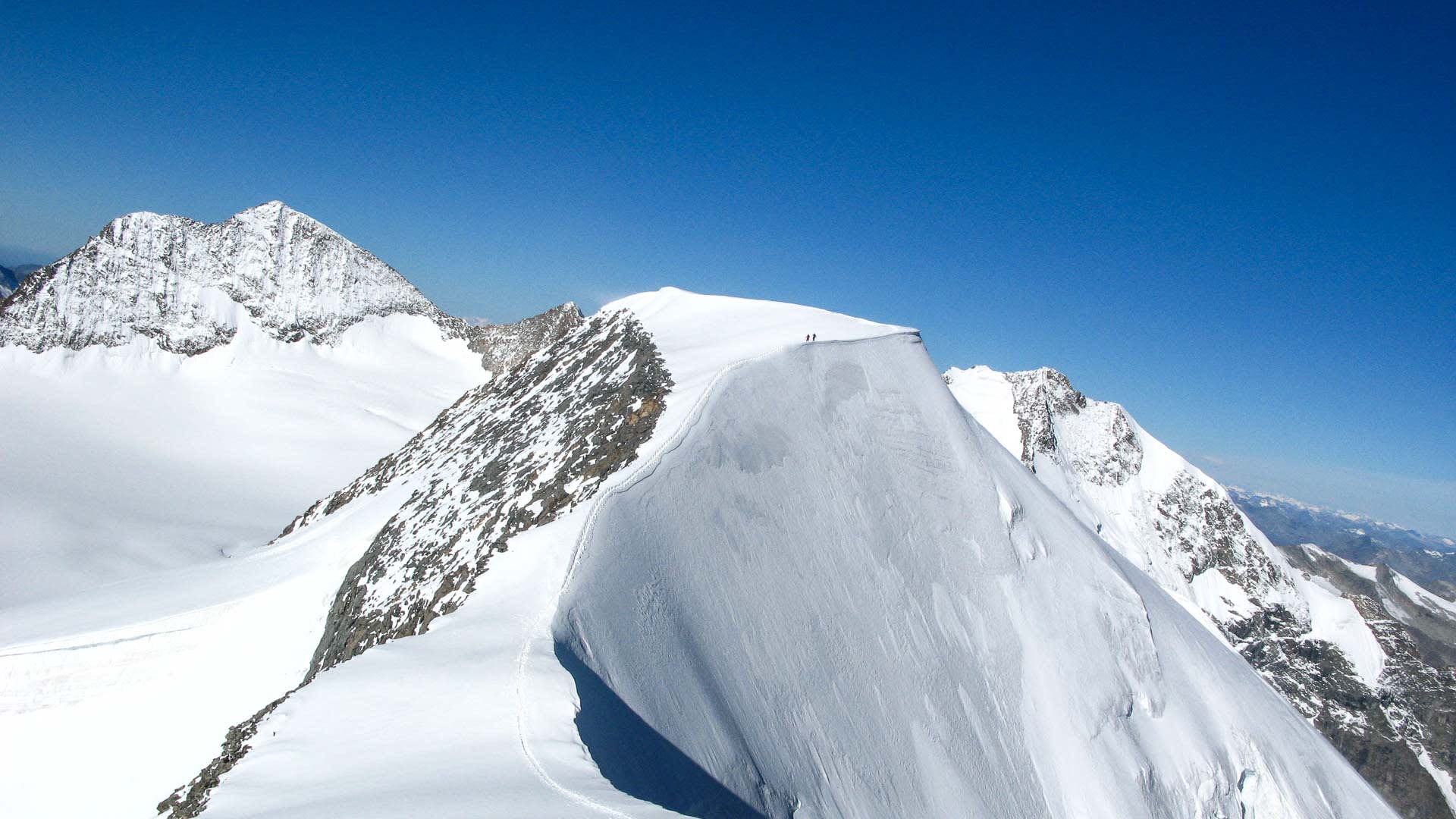 Hochtour Piz Palü: zwei Bergsteiger auf dem Schneegrat mit markanter Wechte und schneebedecktem Gipfel im Hintergrund.