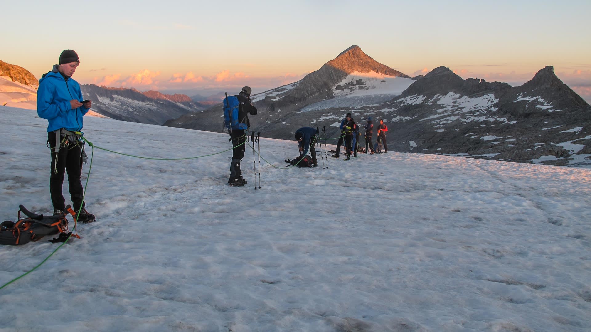 Fünf Bergsteiger am Seil auf dem Gletscherfeld beim Großvenediger, im Hintergrund schneebedeckte Gipfel im Morgenrot.
