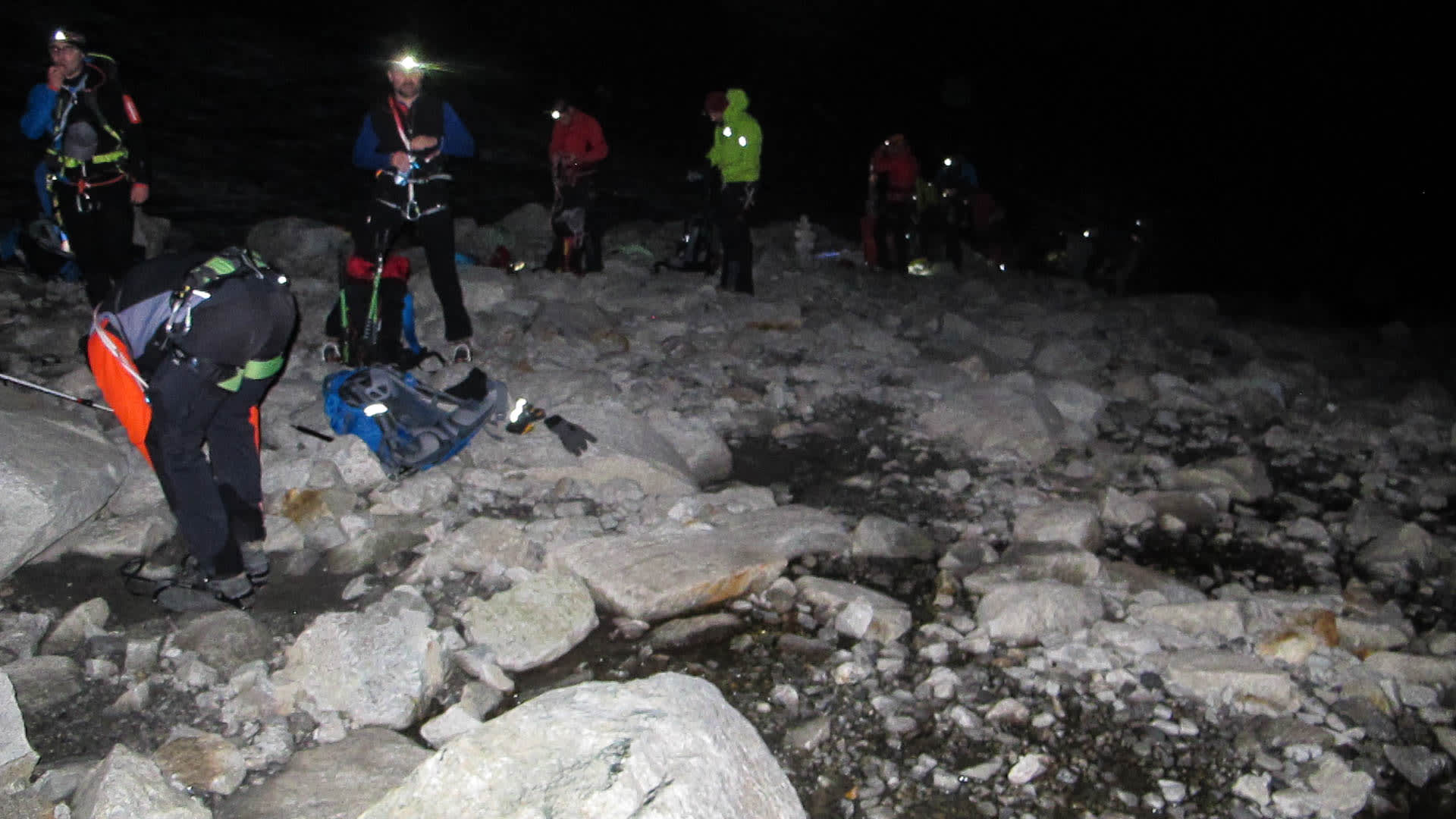 Hochtour am Großvenediger: Bergsteigergruppe legt nachts mit Stirnlampen auf felsigem Gelände Steigeisen an.