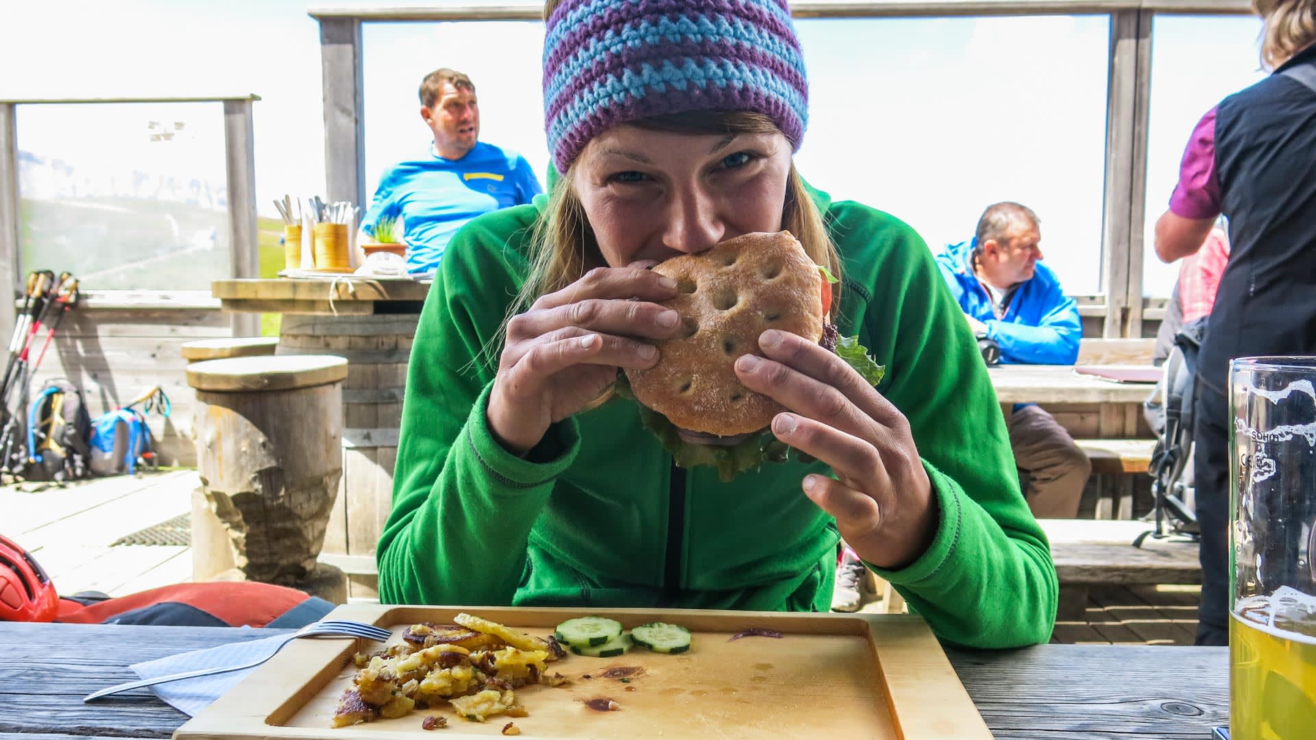 Klettern in den Dolomiten: Kletterin bei der Brotzeit auf der Plattkofel-Hüttenterrasse mit Wanderstöcken im Hintergrund.