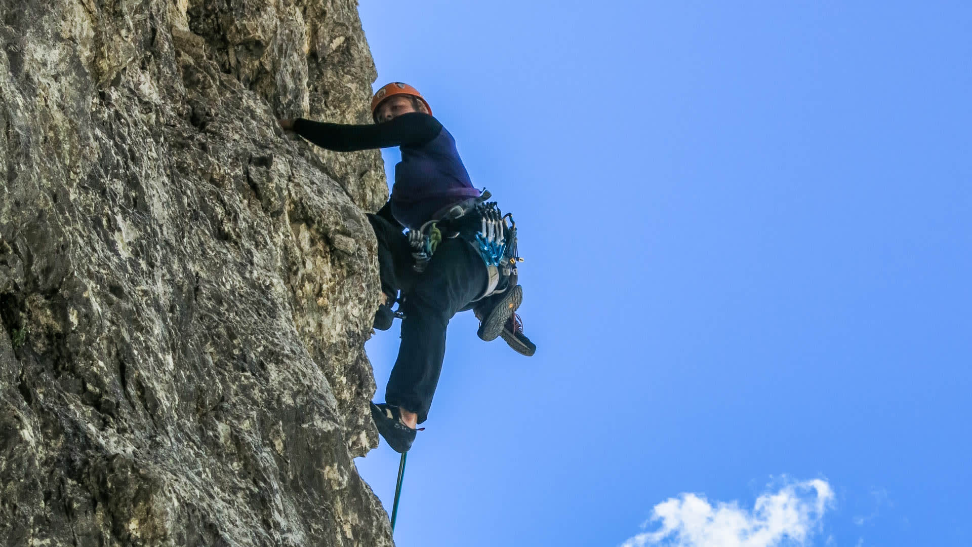 Kletterer mit orangem Helm in Froschperspektive an senkrechter Kalksteinwand am zweiten Sellaturm am Sellapass.