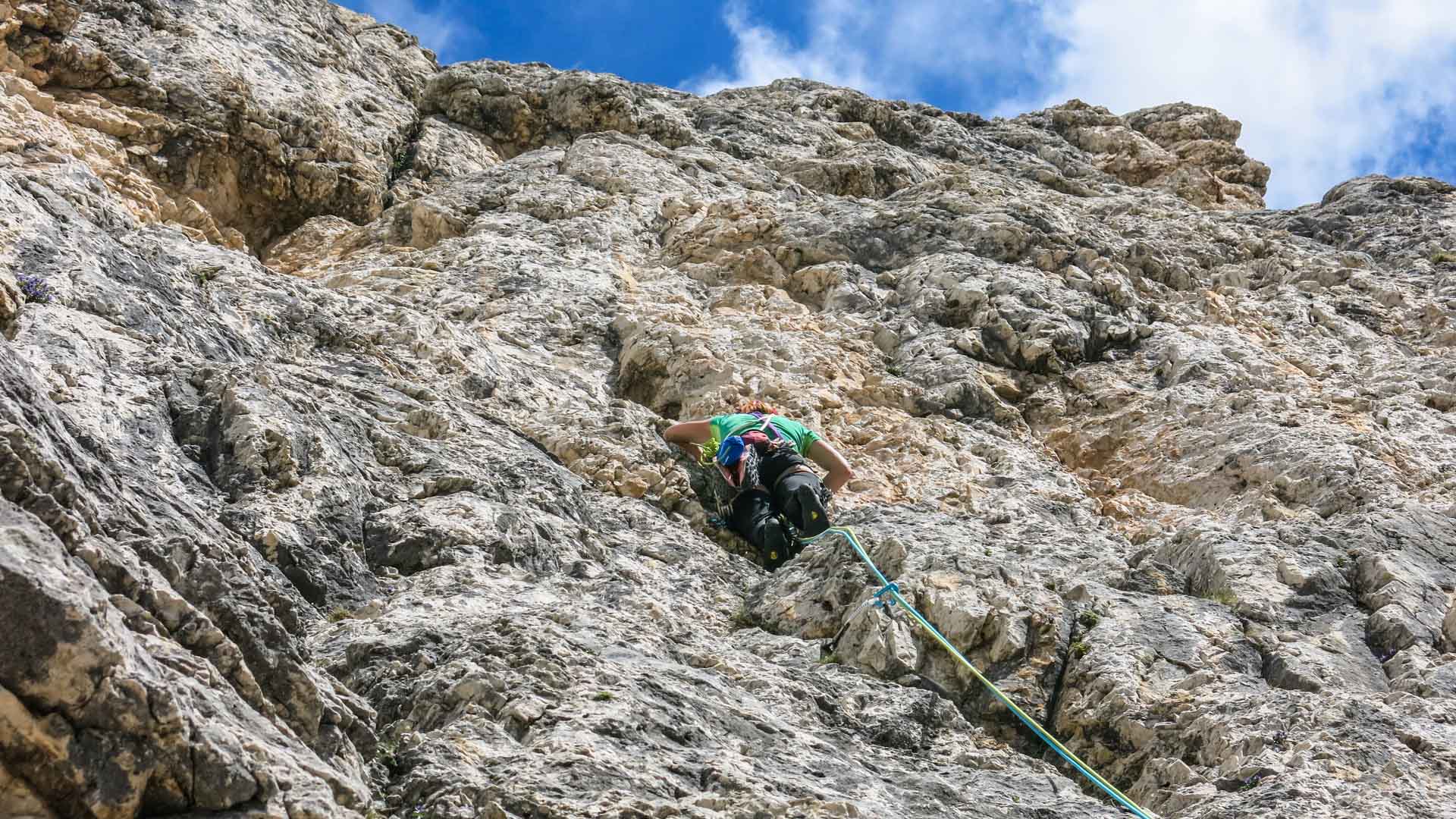 Kletterer mit blauem Helm und Rucksack an der Kalksteinwand der Vajolet Türme im Rosengarten.