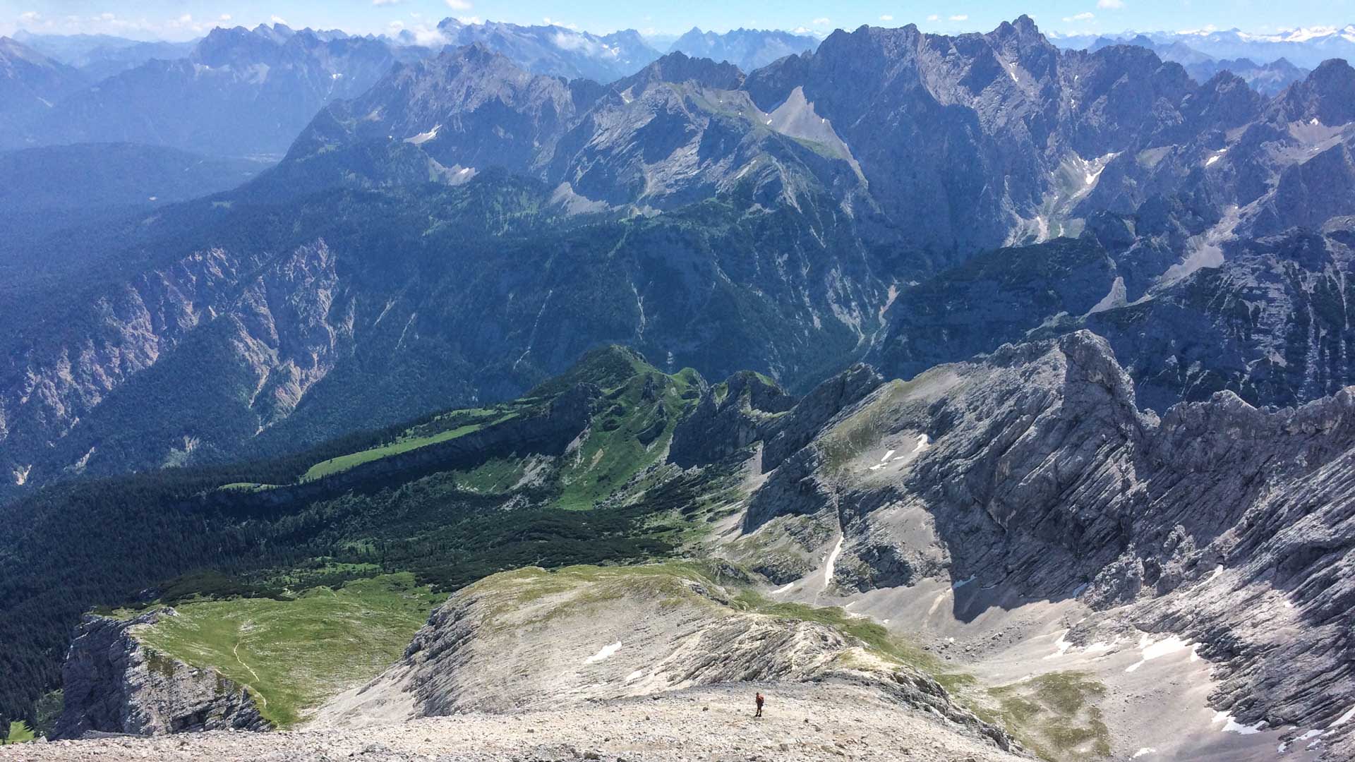 Klettersteig an der Alpspitze: Klettersteiggeher mit rotem Rucksack auf felsig-schotterigem Grat im Sommer.