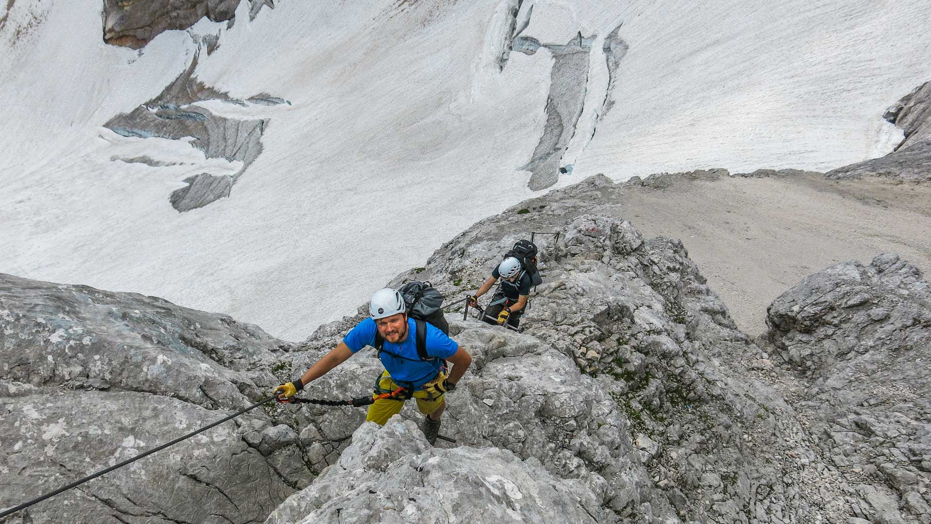 Zwei Personen beim Klettersteig im Höllental zur Zugspitze: vordere Person mit weißem Helm und gelbem Hose am fixierten Drahtseil