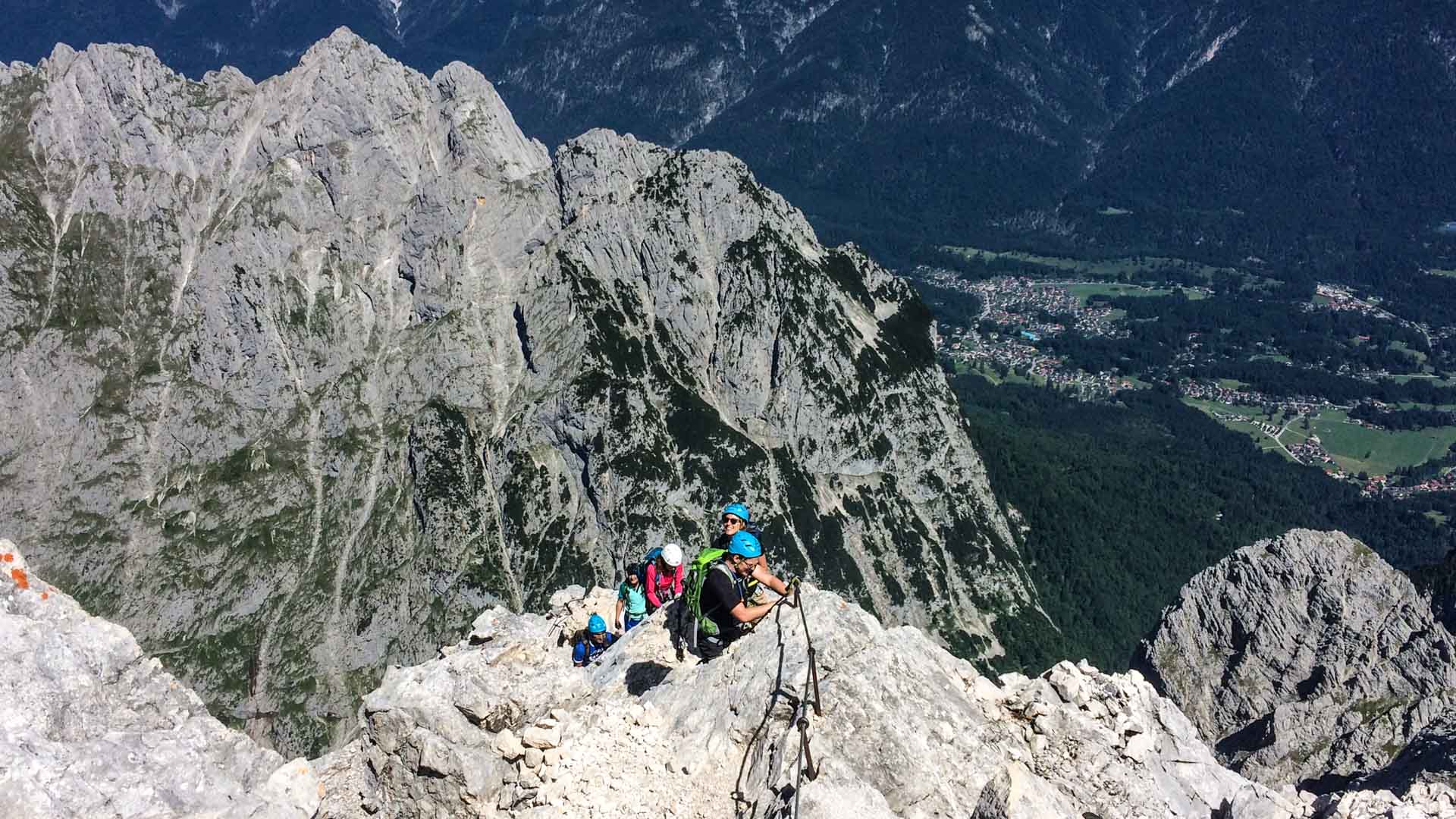 Klettersteig an der Alpspitze: Fünf Klettersteiggeher mit Helmen und Gurten steigen gesicherten Steilgrat auf.