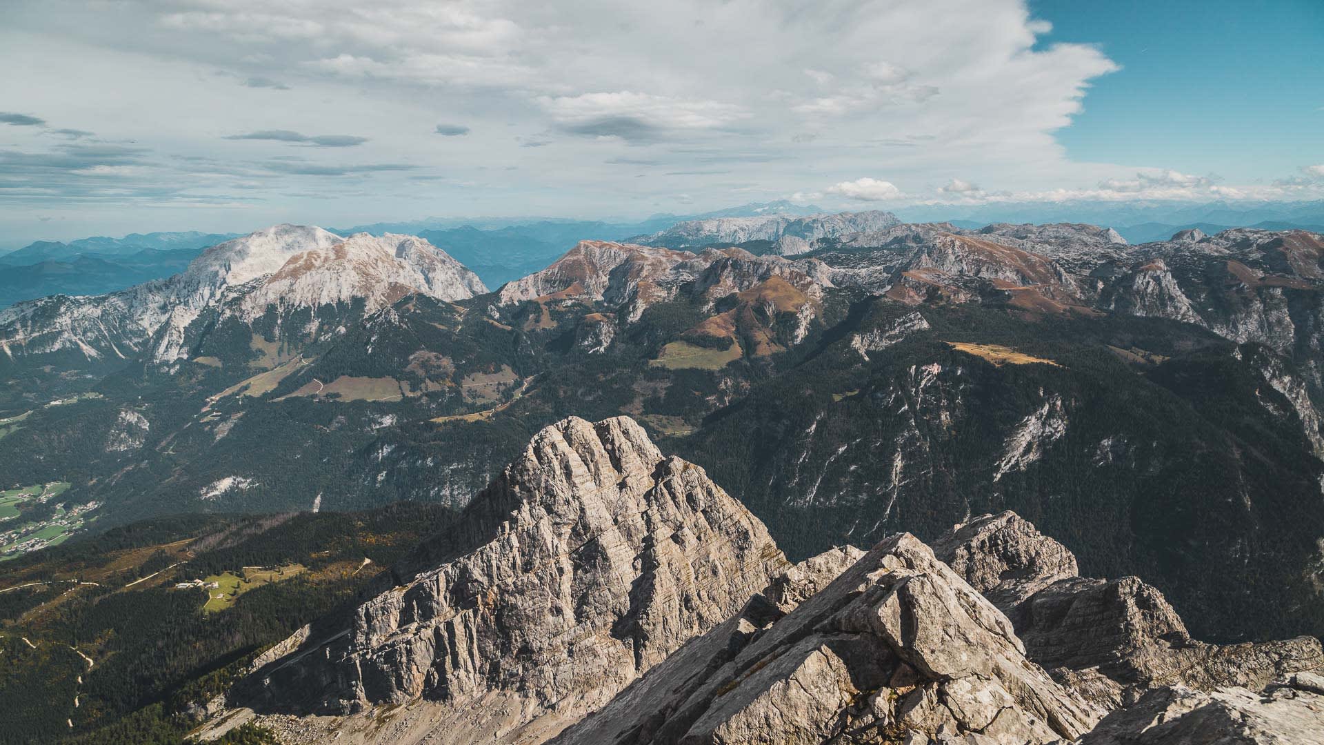 Klettersteig am Watzmann: Weitwinkel-Panorama vom Grat auf hellgraue Kalkfelsen, bewaldetes Tal mit herbstlichen Verfärbungen