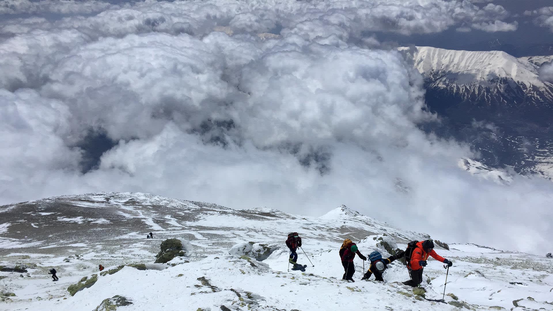Mehrere Skitourengeher steigen mit Stöcken und Rucksäcken einen schneebedeckten Hang zum Damavand im Iran auf.