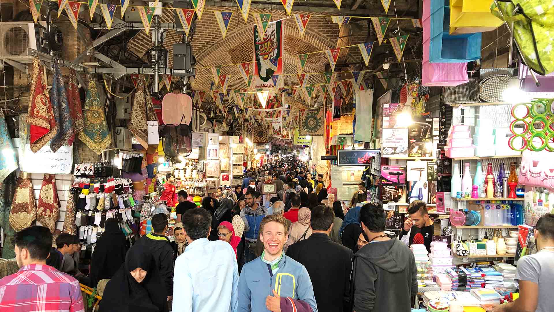 Skitour Iran: Blick in den überdachten Grand Basar in Teheran mit bunten Wimpelketten, Marktständen und zahlreichen Besuchern.
