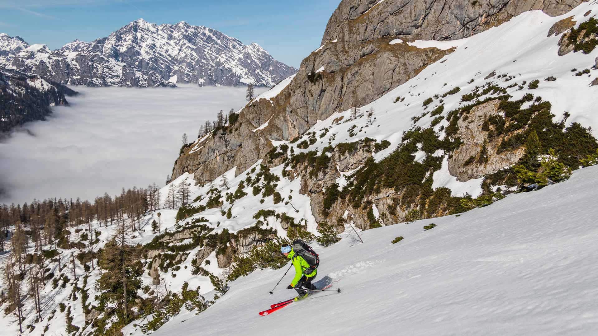 Ein Skitourengeher fährt auf der Großen Reibn ab, im Hintergrund das Watzmann-Massiv über dem Wolkenmeer.