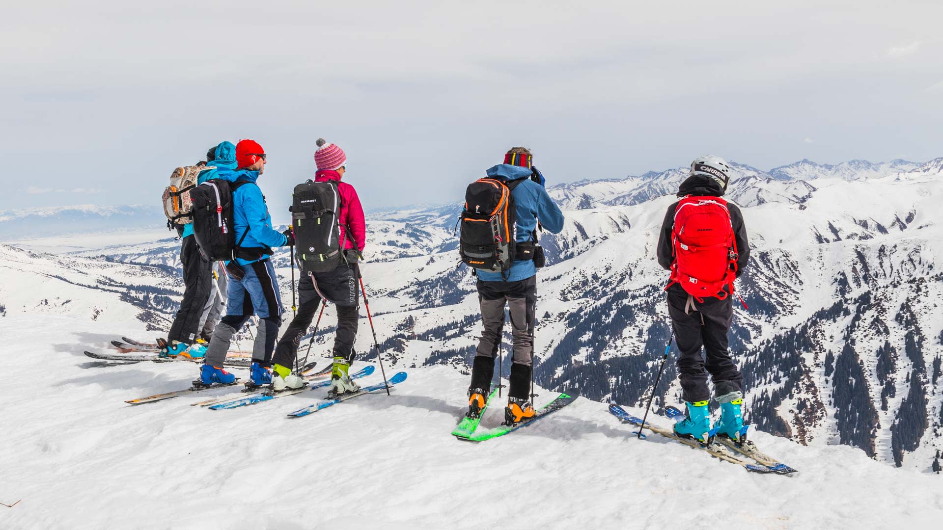 Vier Skitourengeher stehen auf einem Kamm im Skigebiet Jergalan und blicken ins verschneite Bergpanorama.