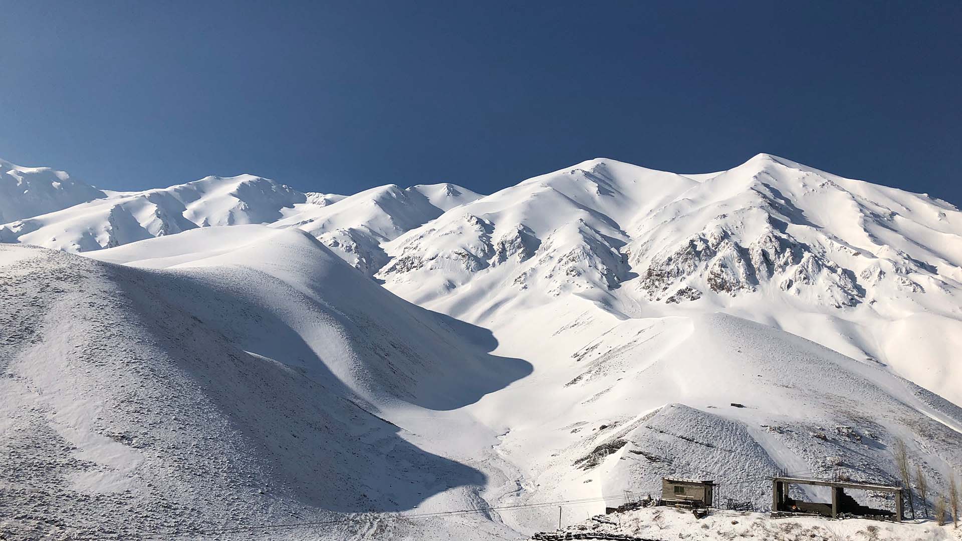 Skitour im Iran: verschneite Hochgebirgslandschaft am Damavand mit gerundeten Gipfeln und Windstrukturen im Schnee.