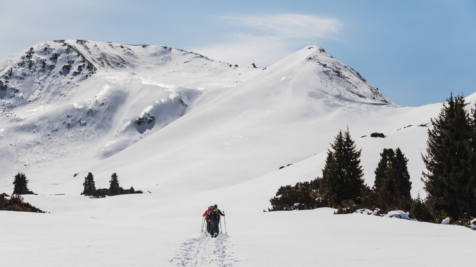 Skitour im Karakol-Gebiet: drei Skitourengeher queren ein schneebedecktes Plateau vor einem zweigipfligen Bergstock.