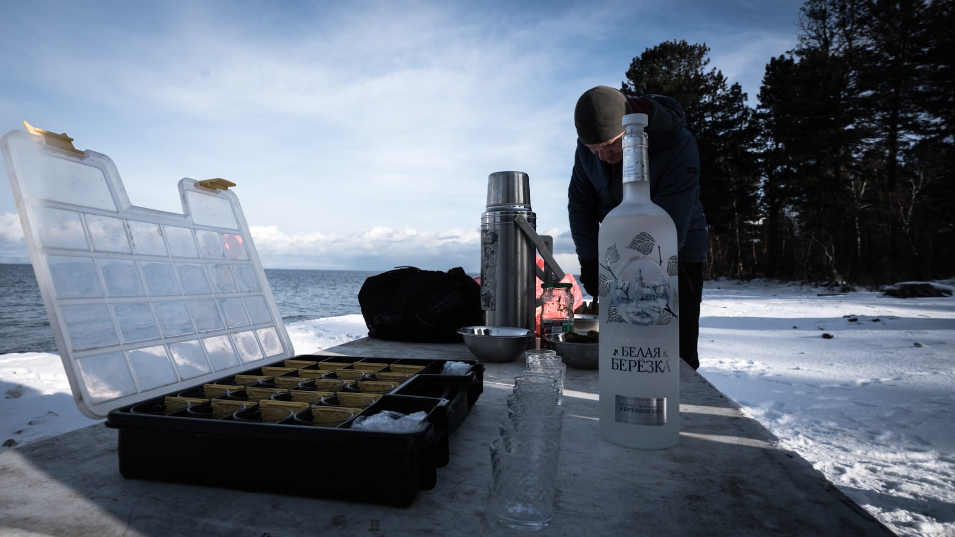 Skitour-Pause am Baikalsee: Wodka-Flasche, Thermoskanne und Angelköder auf einem Tisch im Schnee.