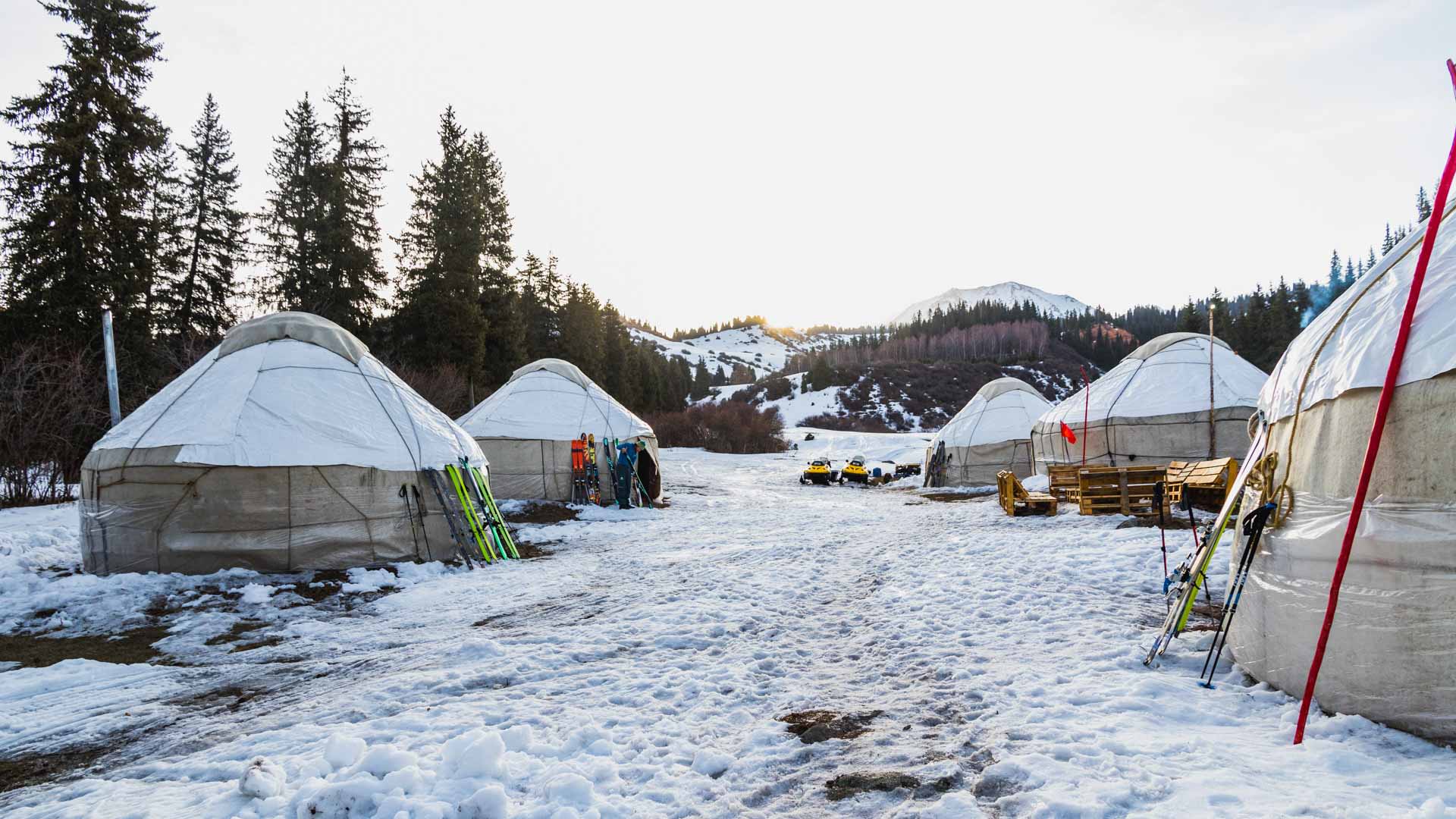 Skitour in Kirgistan: Fünf Jurten als Wintercamp auf schneebedecktem Hang, Tourenski lehnen an den Wänden.