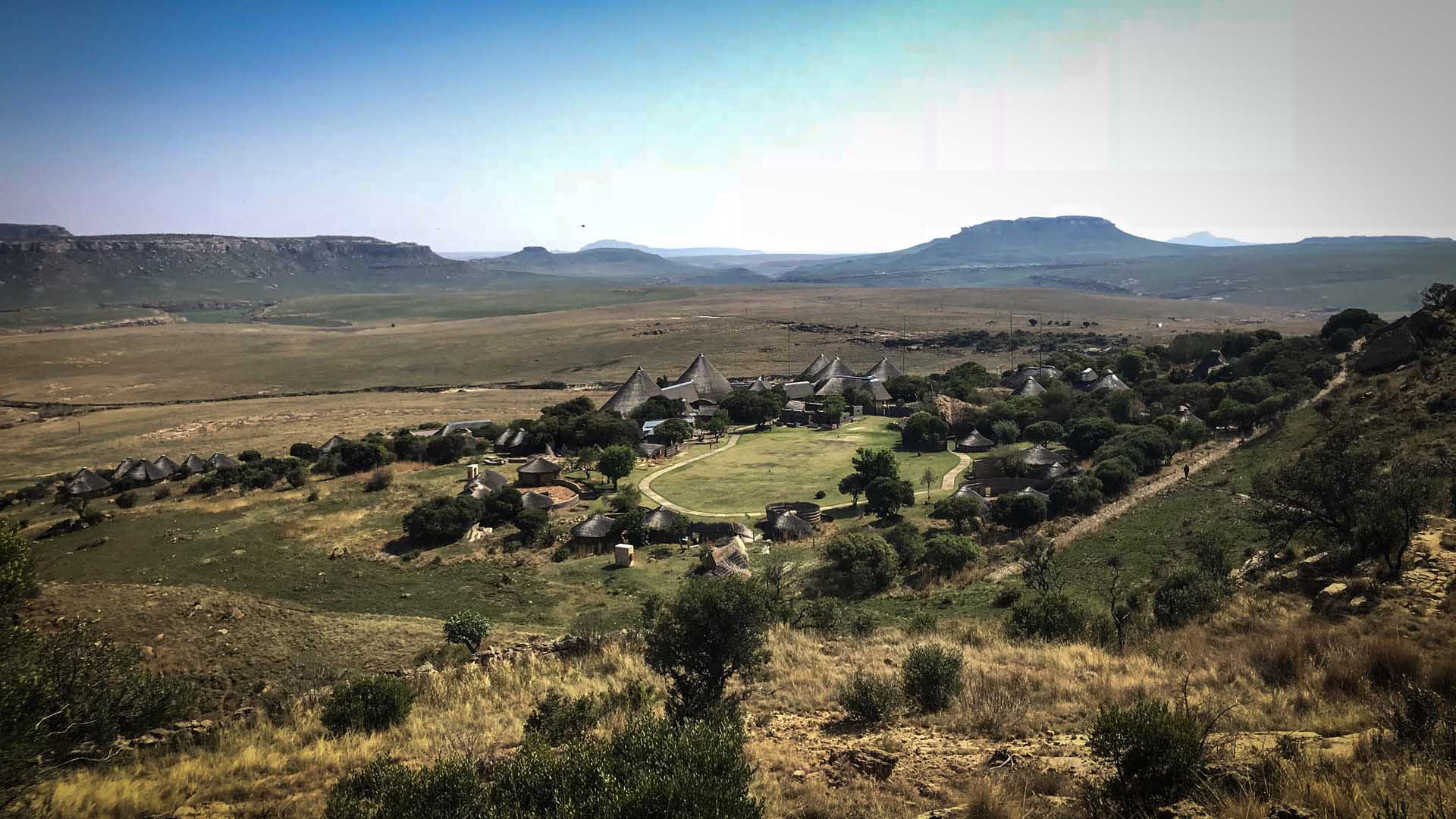 Trekking im Golden Gate Nationalpark: Panoramablick auf ein Basotho-Dorf mit Rundhütten in der Savanne.