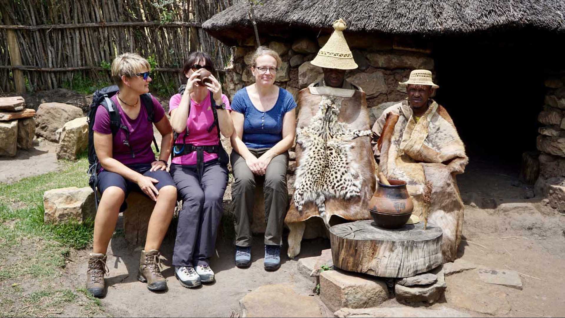 Trekking im Golden Gate Nationalpark: Drei Trekkerinnen sitzen neben zwei traditionell gekleideten Basotho