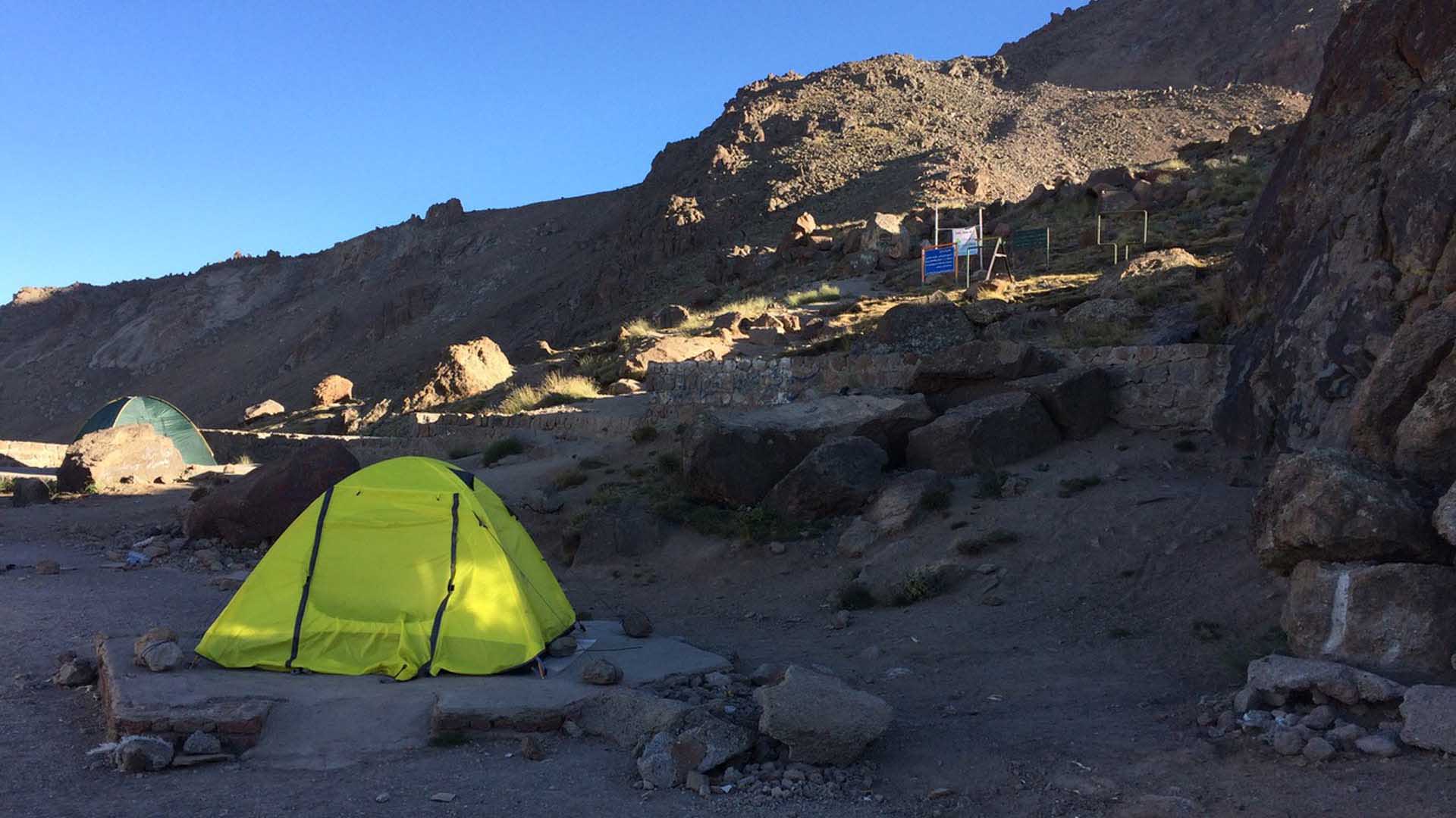 Trekking-Campsite im Iran: gelb-grünes Kuppelzelt auf Steinplatte in felsiger, vegetationsarmer Gebirgslandschaft