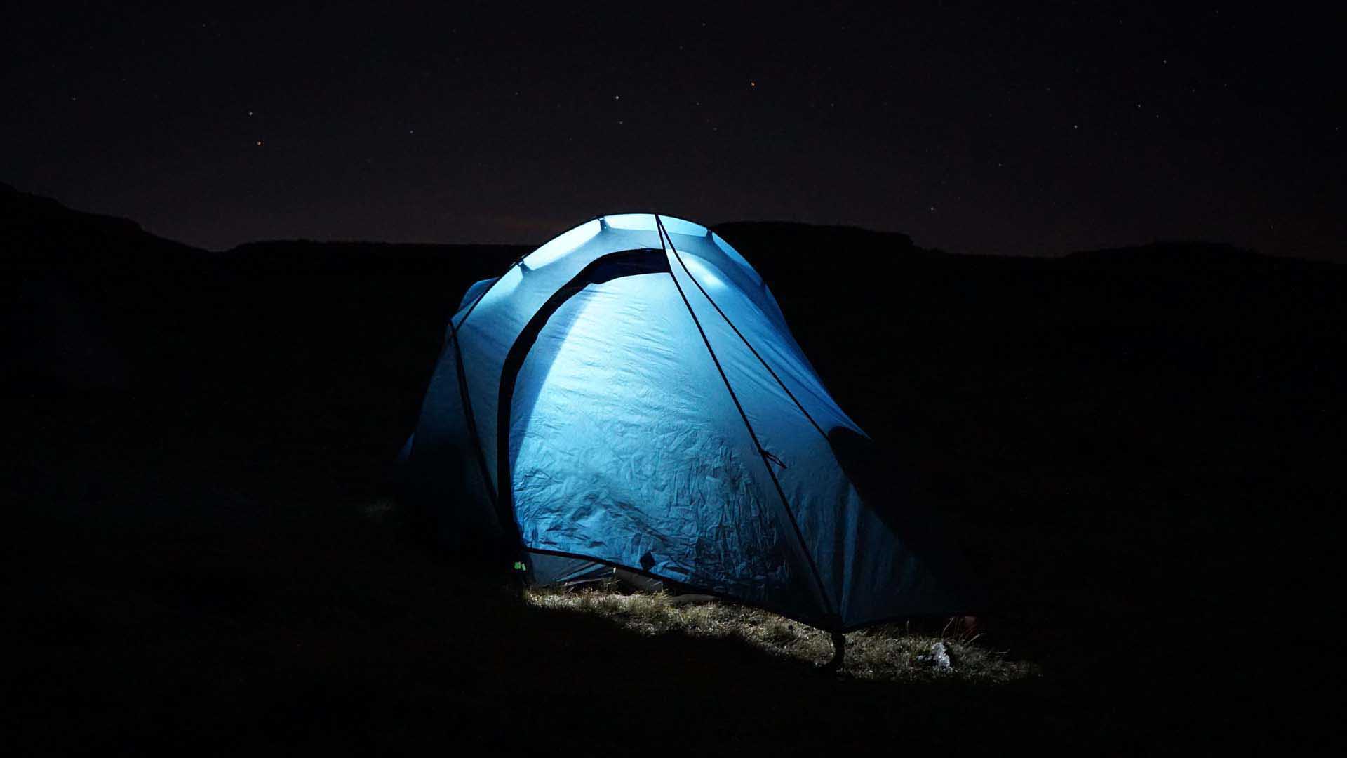 Trekking in den Drakensbergen Südafrika: von innen blau beleuchtetes Kuppelzelt bei Nacht auf Grasboden