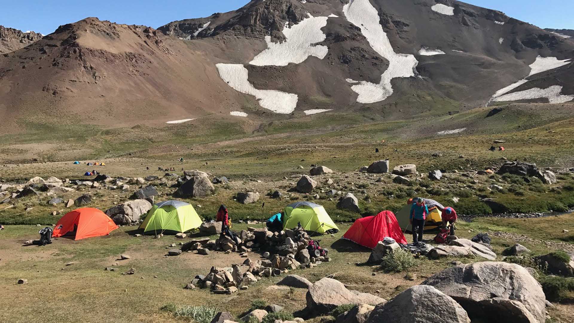 Trekking im Iran: Kleines Basecamp mit fünf Expeditionszelten auf steinigem Plateau vor dunklem Vulkankegel