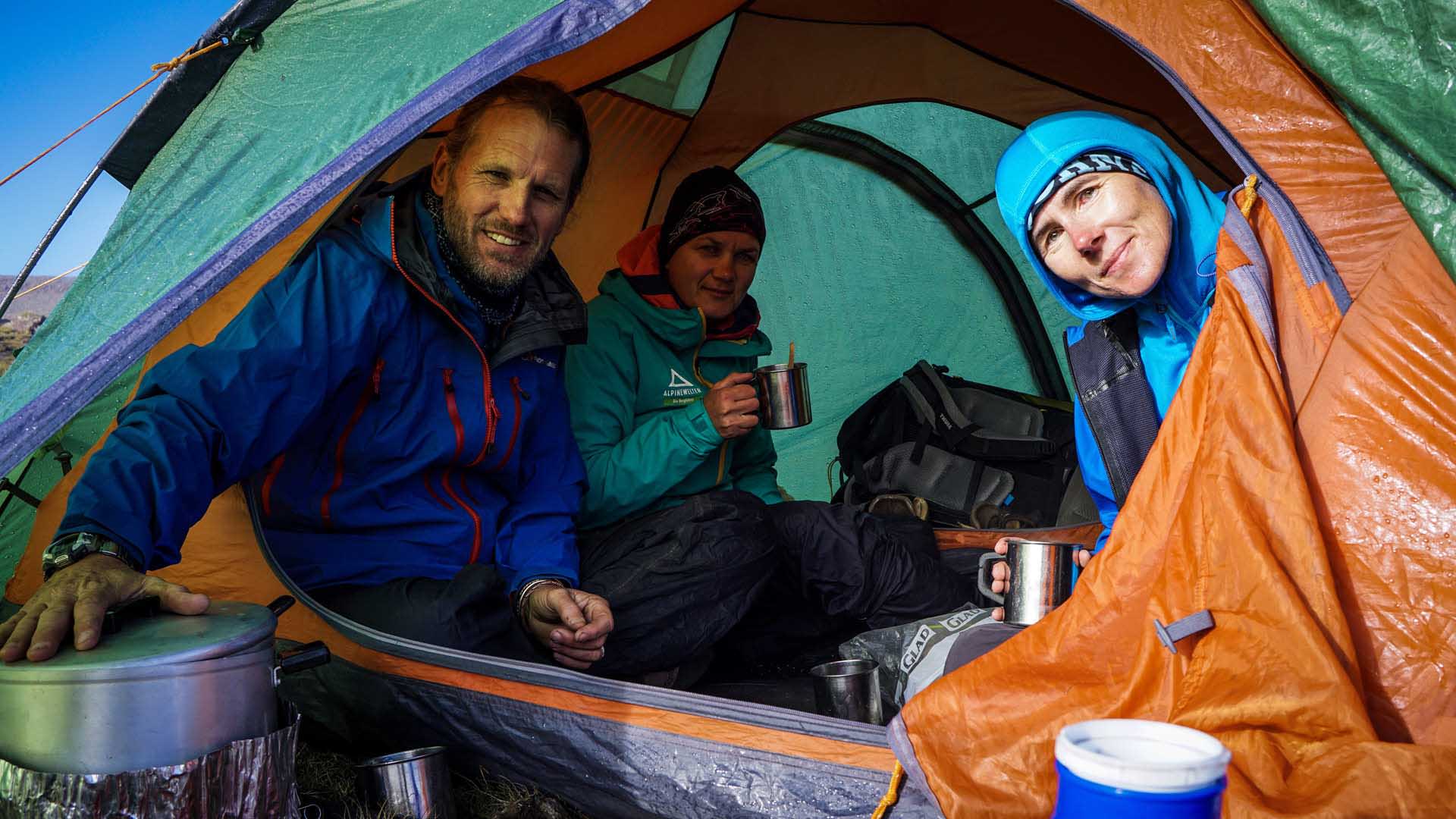 Trekking in den Drakensbergen: drei Trekker pausieren im Küchenzelt mit Campingbechern und Kochtopf im Vordergrund.