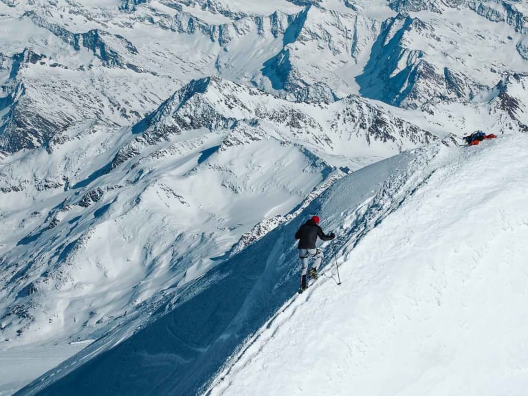 Skitourengeher steigt den Gipfelgrat des Großvenedigers auf, am Skidepot liegen Rucksäcke im Schnee.