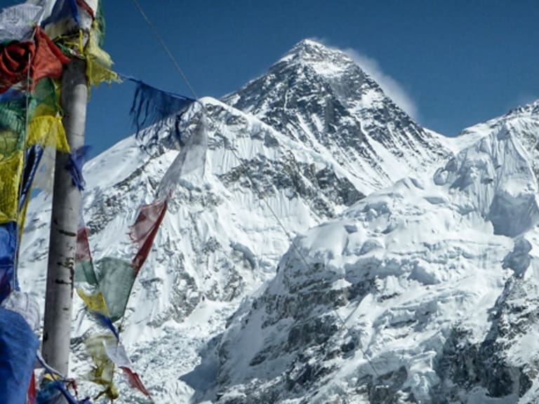 Trekking in der Khumbu-Region: bunte Gebetsfahnen an einem Mast mit Blick auf den vergletscherten Mount Everest.