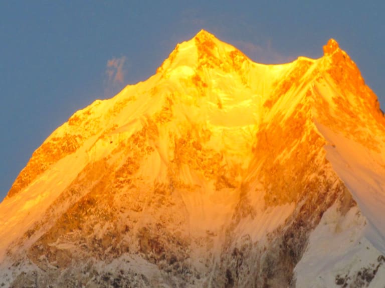 Trekking am Manaslu: pyramidenförmiger Achttausender in orange-goldenem Abendlicht, Schnee- und Eisflanken