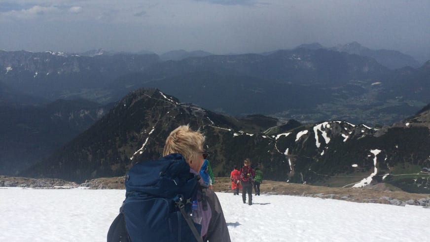 Gruppe von Bergwanderern beim Abstieg vom Schneibstein über einen schneebedeckten Hang mit Blick auf weitläufige Bergketten