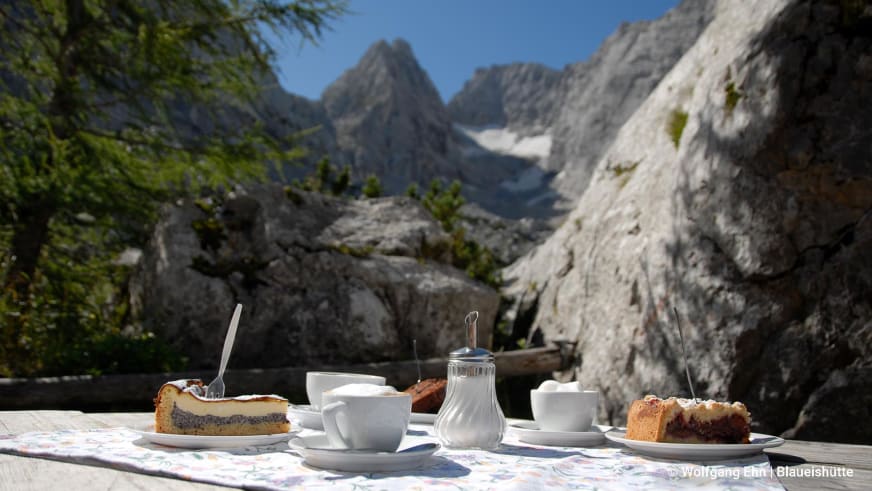 Bergwanderung zur Blaueishütte Berchtesgaden: Kaffeegedeck mit Kuchen auf der Hüttenterrasse vor Kalkfelswand.