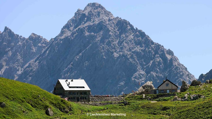 Bergwanderung zur Pfälzerhütte in Liechtenstein mit Berghaus auf Plateau und Felsgipfel im Hintergrund.