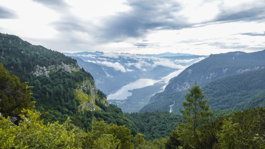 Blick von erhöhter Position auf einen lang gestreckten Gebirgssee im Tal unterhalb des Vrh Planje in Slowenien.