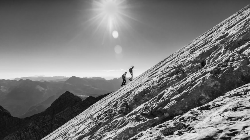 Bergwanderung auf der Watzmann Wiederroute: zwei Bergwanderer steigen eine steile Felsplatte am Wiederband auf.