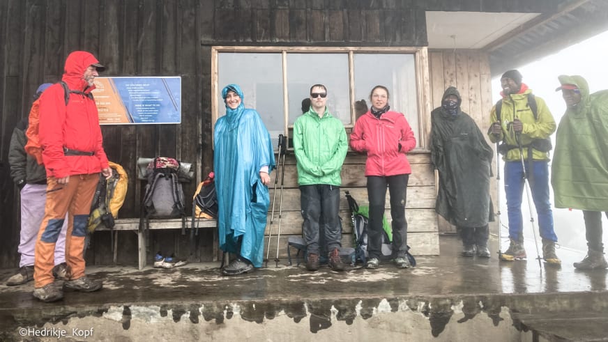 Acht Höhenbergsteiger pausieren bei Regen und Nebel auf einer Veranda am Mweka Camp am Kilimanjaro.