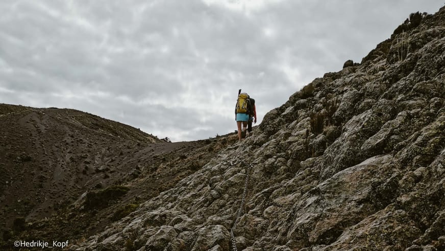Höhenbergsteiger klettert mit Metallkette als Hilfslinie an einem steilen Vulkanfelsen am Mount Meru.