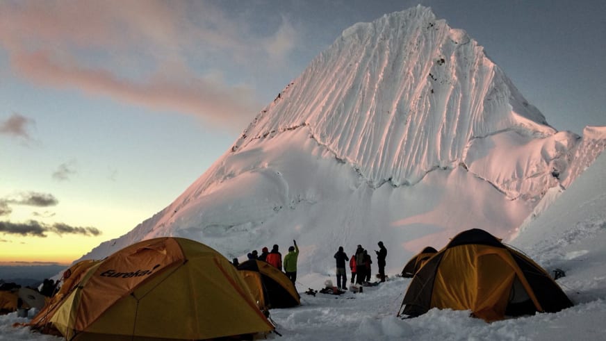 Expedition Alpamayo: Gruppe Höhenbergsteiger im Hochlager mit Zelten vor der vergletscherten Gipfelflanke.